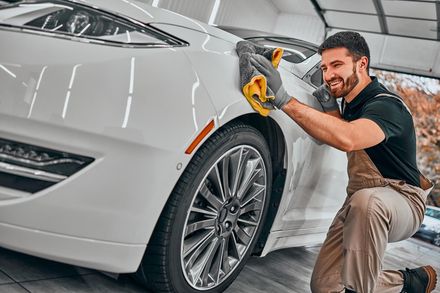 Detailer polishing a white car in a garage with a yellow cloth