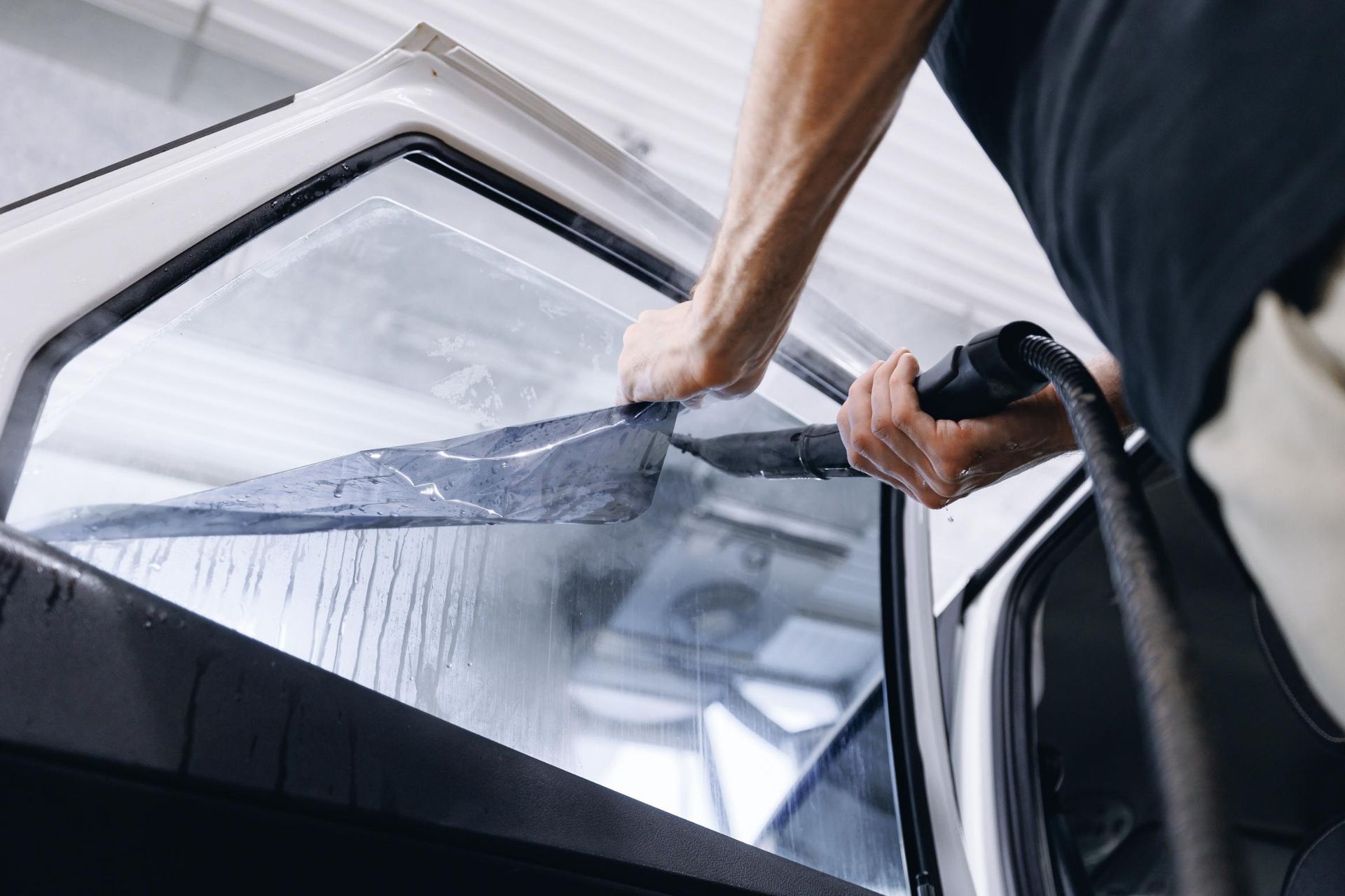 Person cleaning a car windshield with a squeegee from inside the vehicle