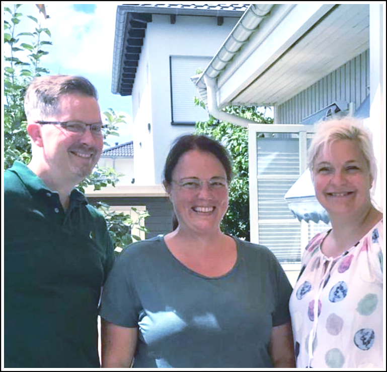 Ein Mann und zwei Frauen posieren für ein Foto vor einem Haus