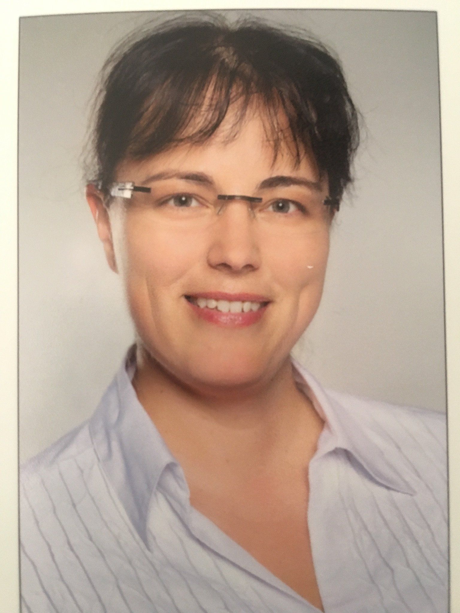 Eine Frau mit Brille und gestreiftem Hemd lächelt in die Kamera.