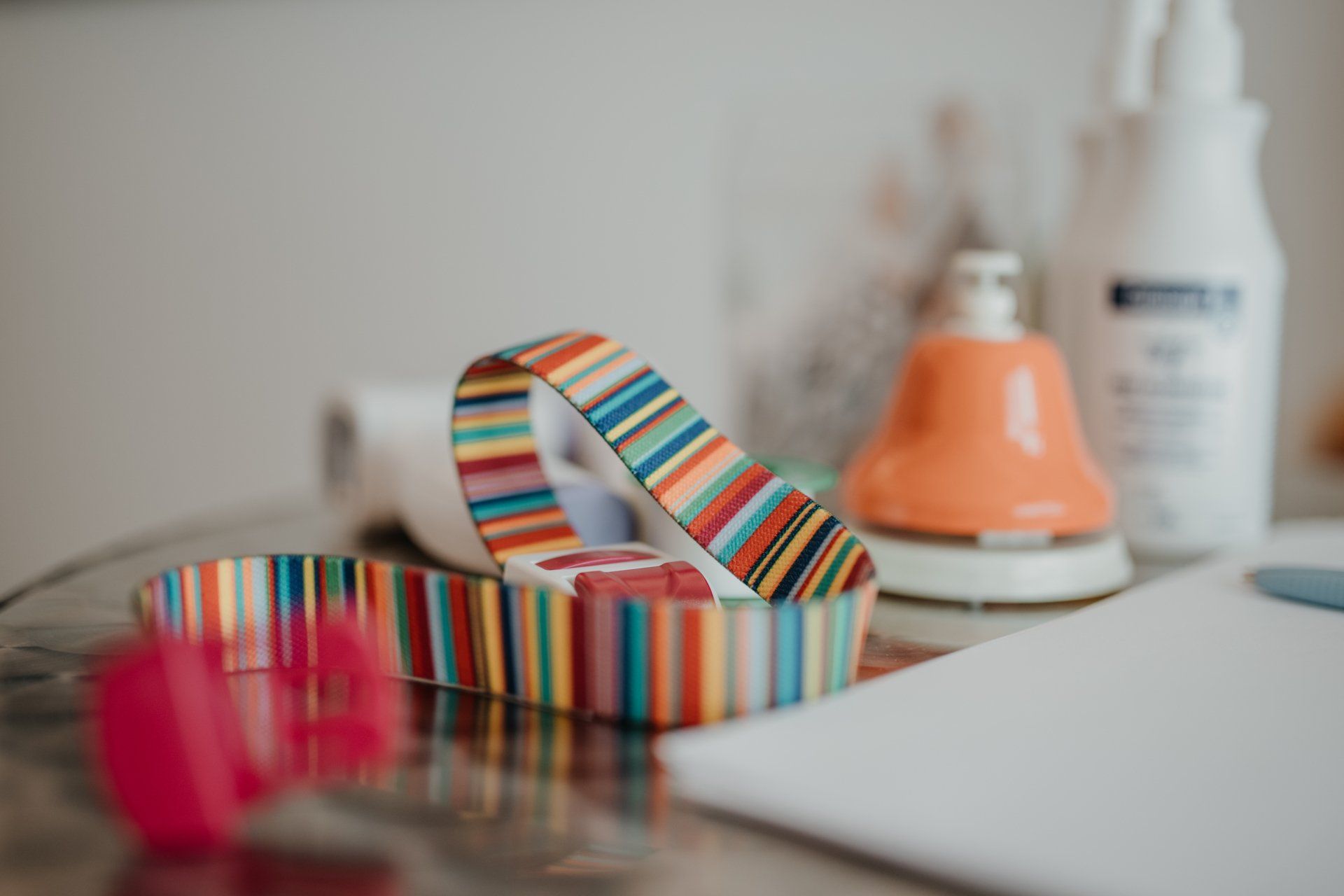 Auf einem Tisch liegt neben einer Flasche Klebstoff ein bunt gestreiftes Band.