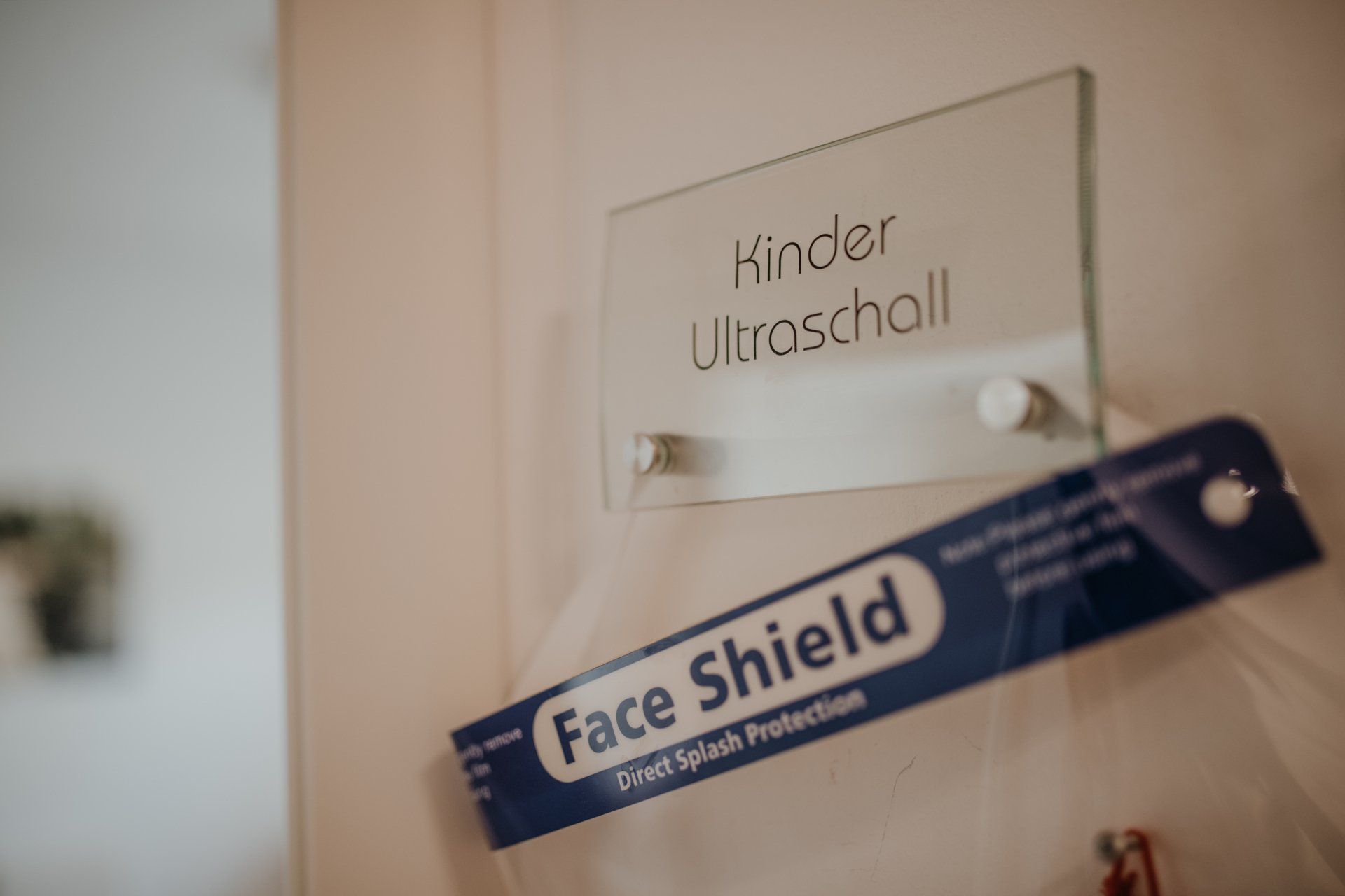 An einer Wand hängt neben einem Schild ein Gesichtsschutz.