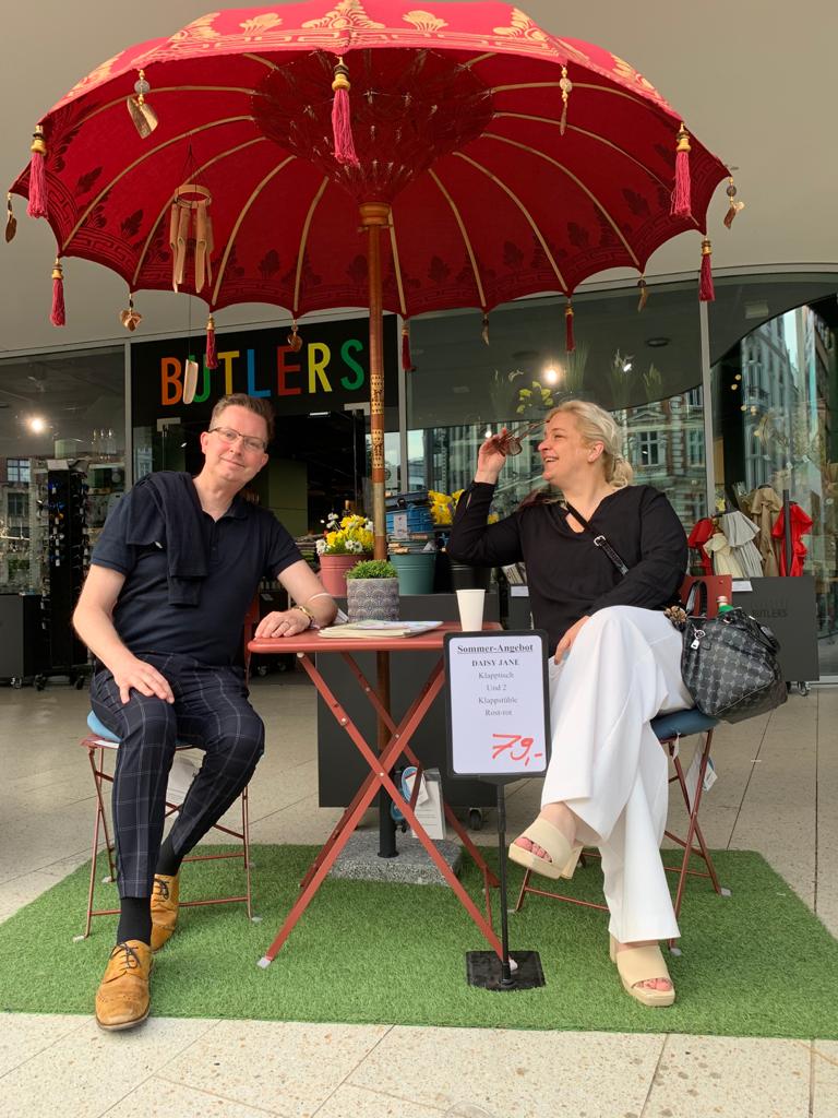 Ein Mann und eine Frau sitzen unter einem Sonnenschirm an einem Tisch.