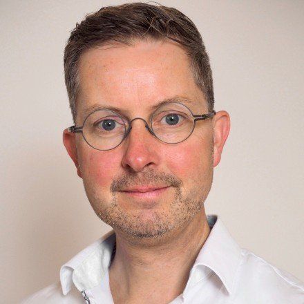 Ein Mann mit Brille und weißem Hemd lächelt in die Kamera.