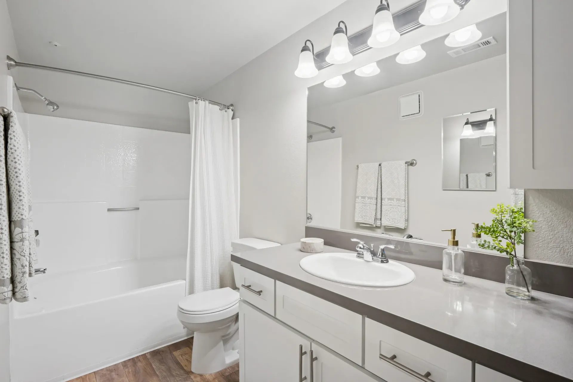 Modern apartment bathroom with white tub/shower, shower curtain, vanity, sink, mirror, and towels.