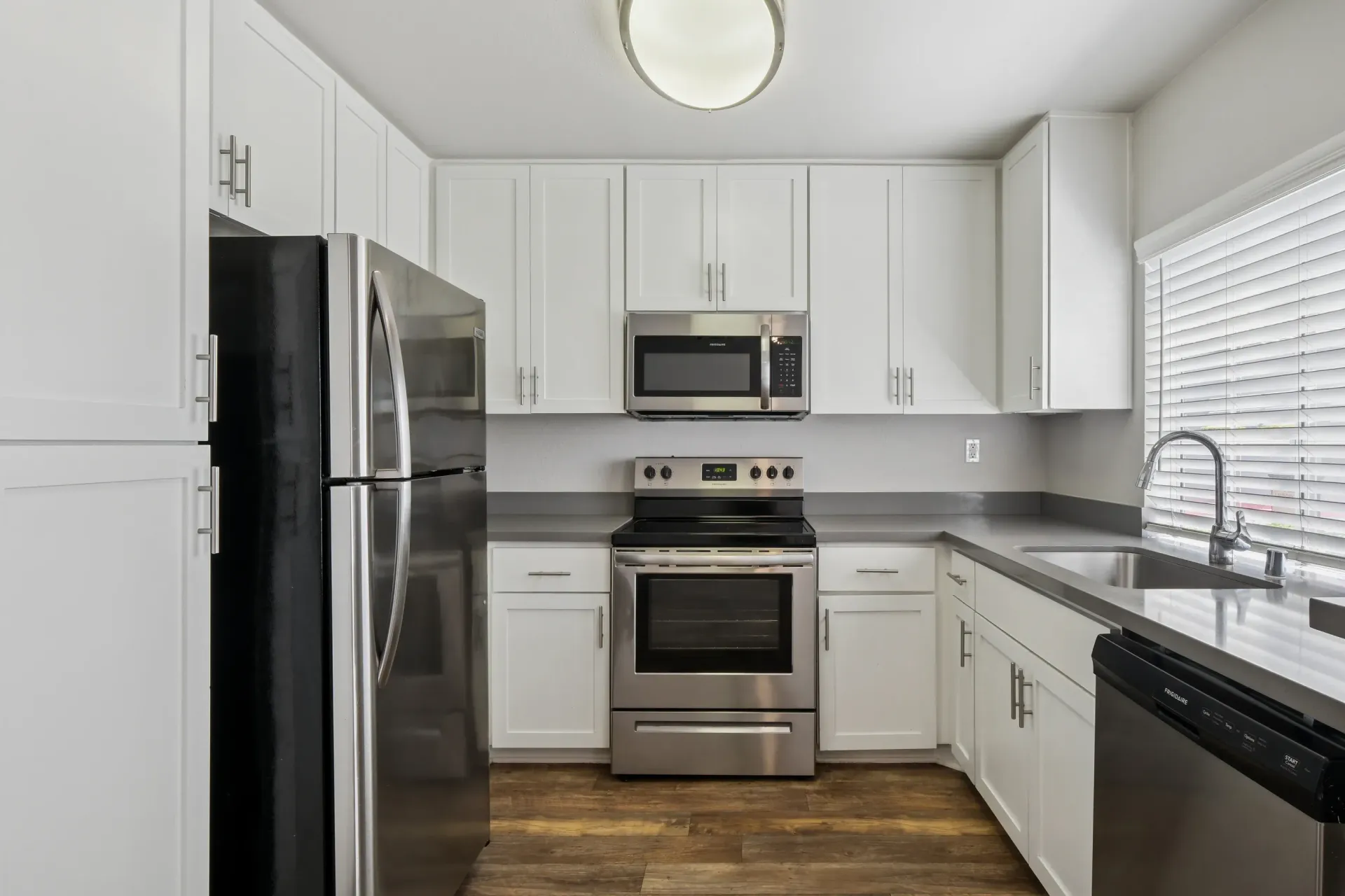 White kitchen with stainless steel appliances and a window above the sink.