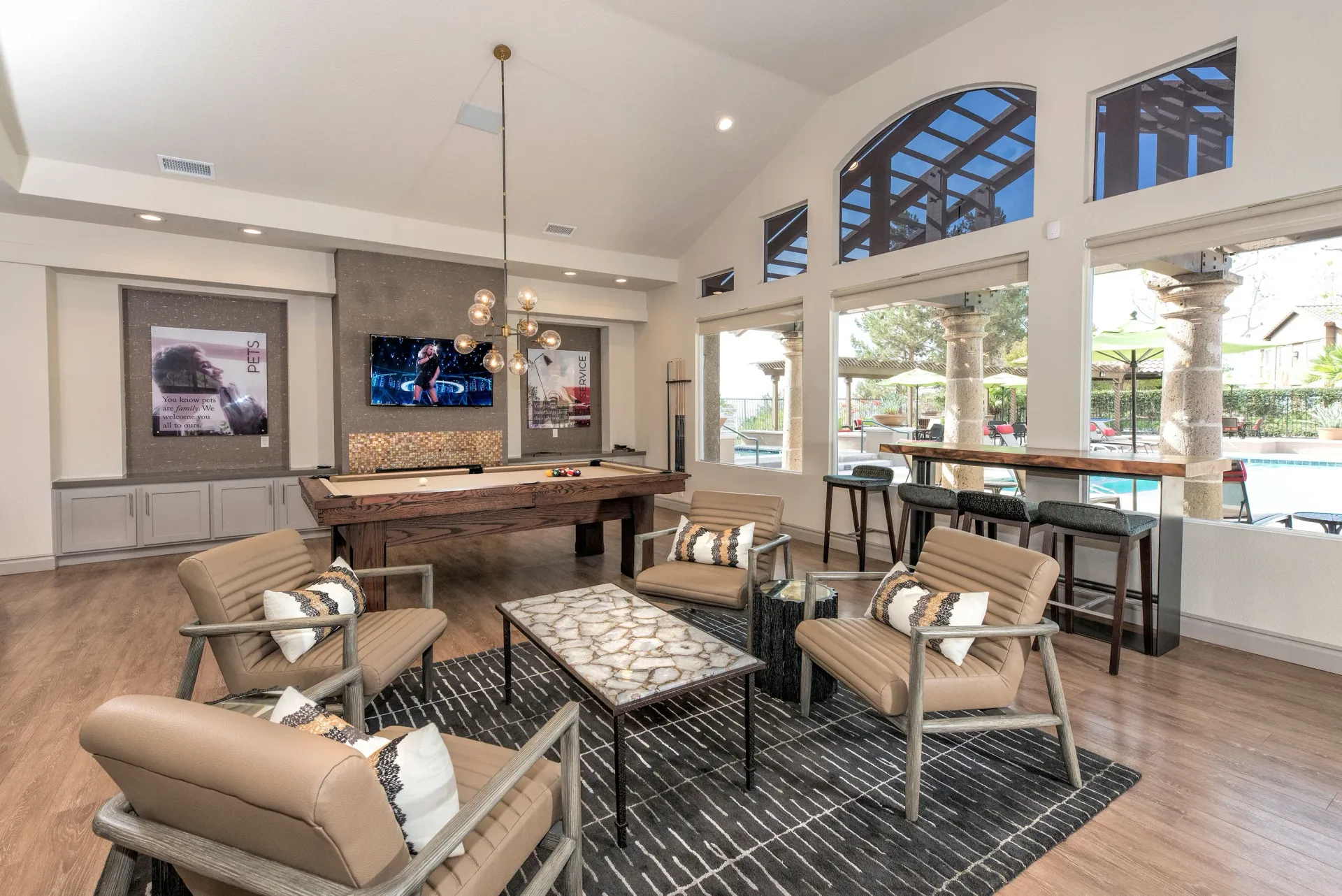 Indoor community lounge with a pool table, comfortable seating, and large windows overlooking the outdoor pool.