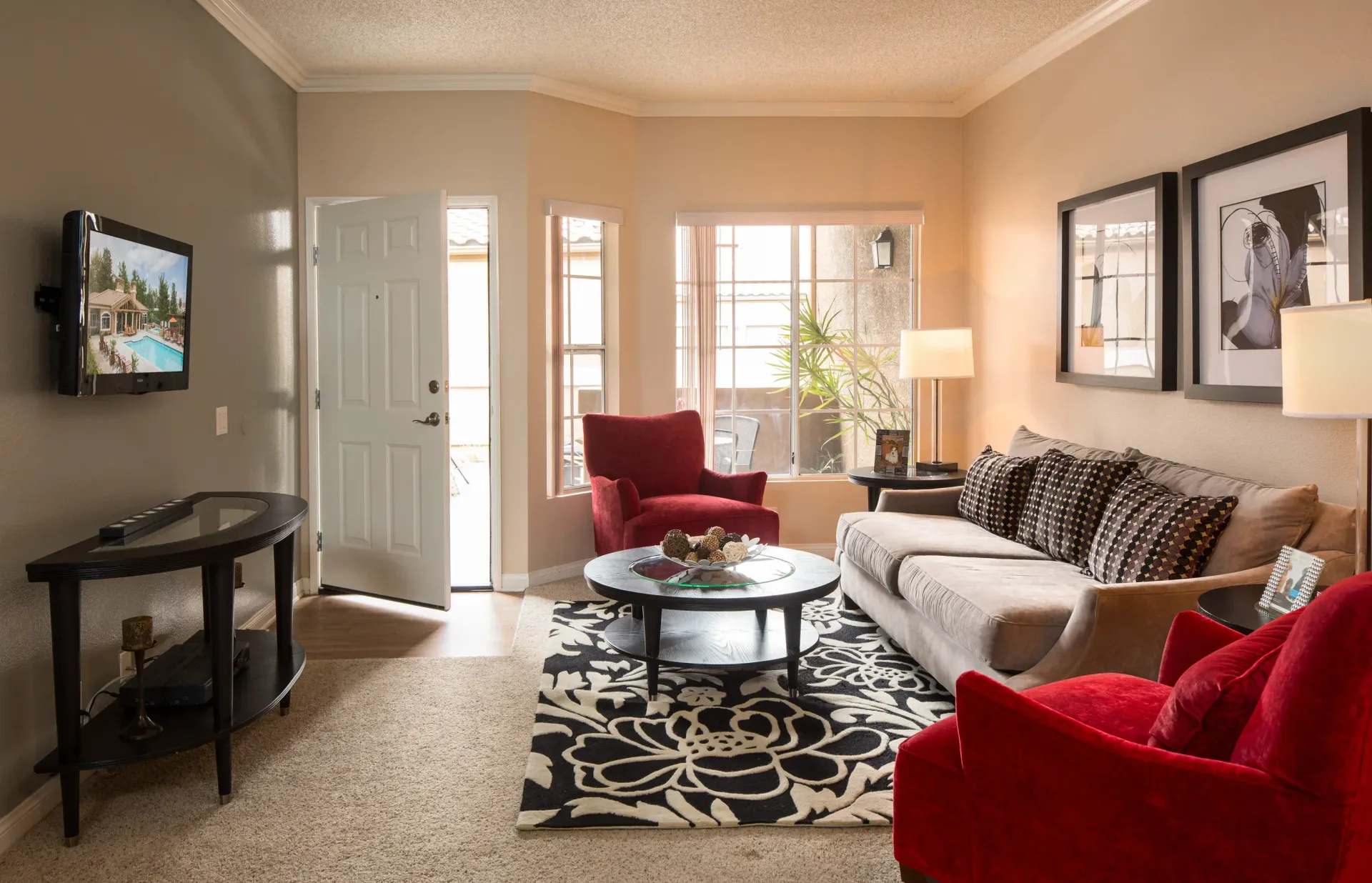 Cozy apartment living room with beige walls, a gray sofa, red chairs, and a round coffee table.
