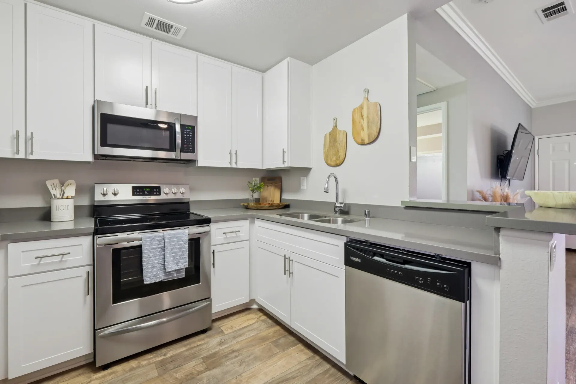Modern white kitchen with stainless steel range, microwave, dishwasher, double sink, and gray countertops.