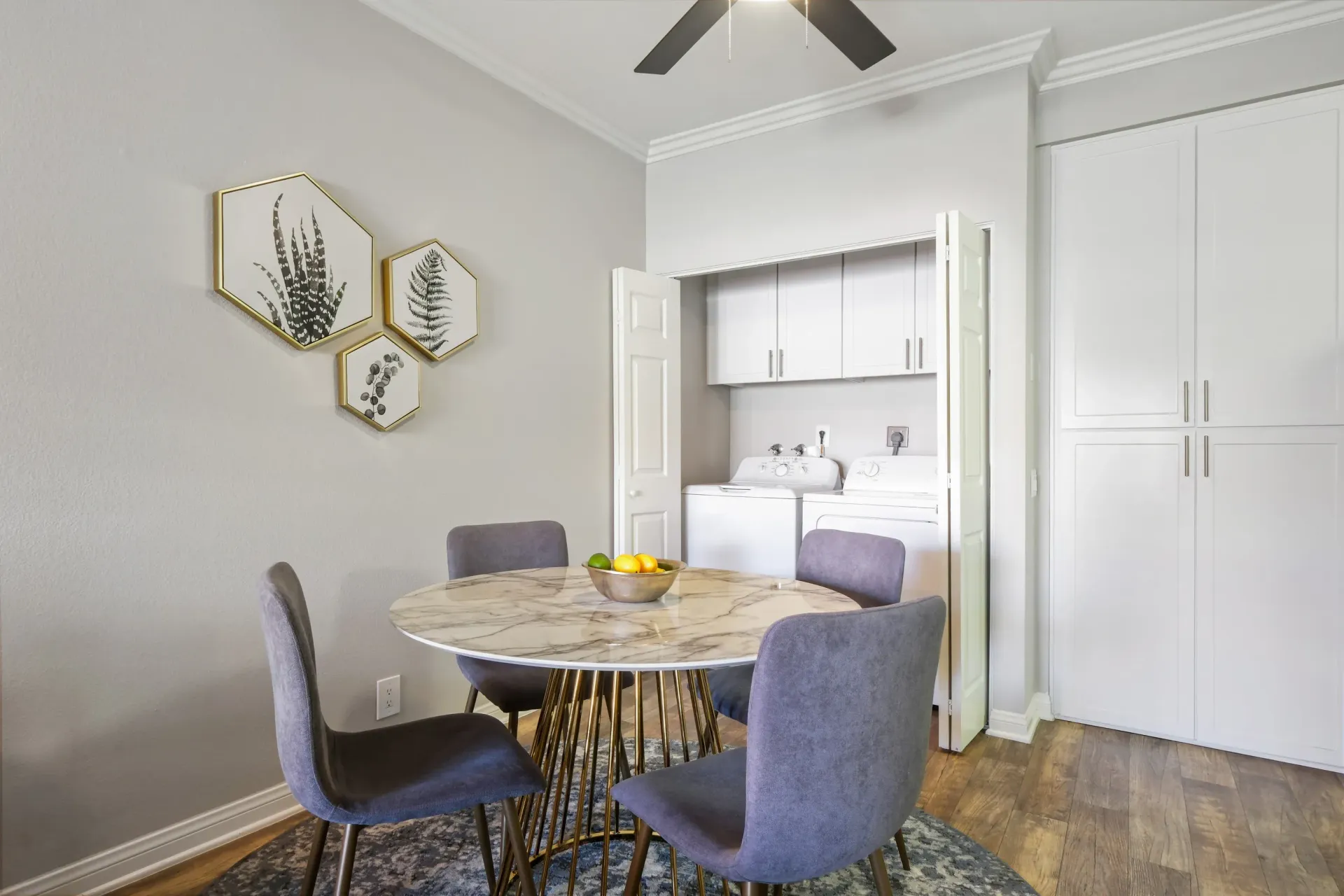 Dining area with round marble table and four purple chairs; laundry closet with washer and dryer in the background.