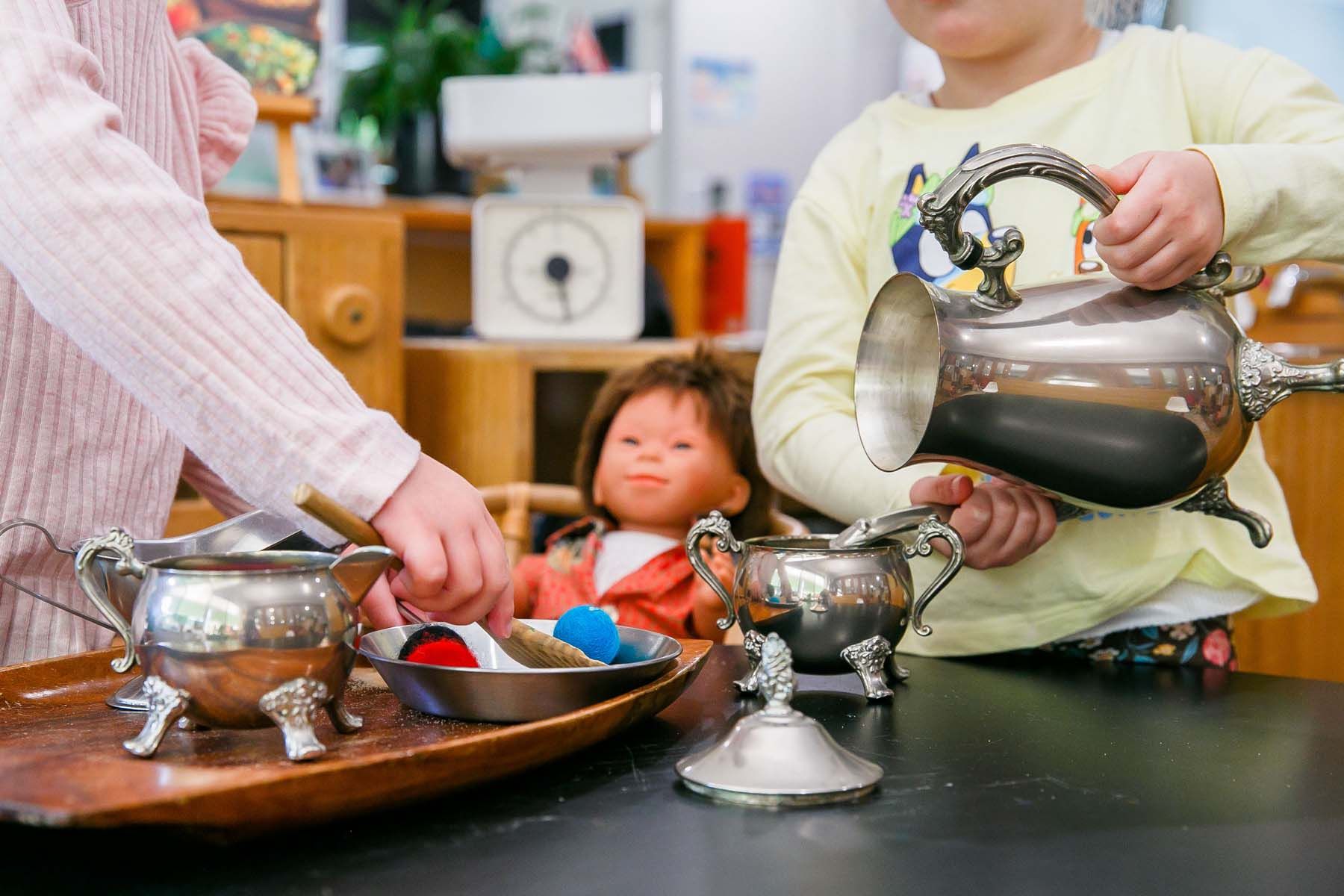 Two children are playing with silverware and a doll on a table. — Killarney Vale Preschool In Tumbi Umbi, NSW