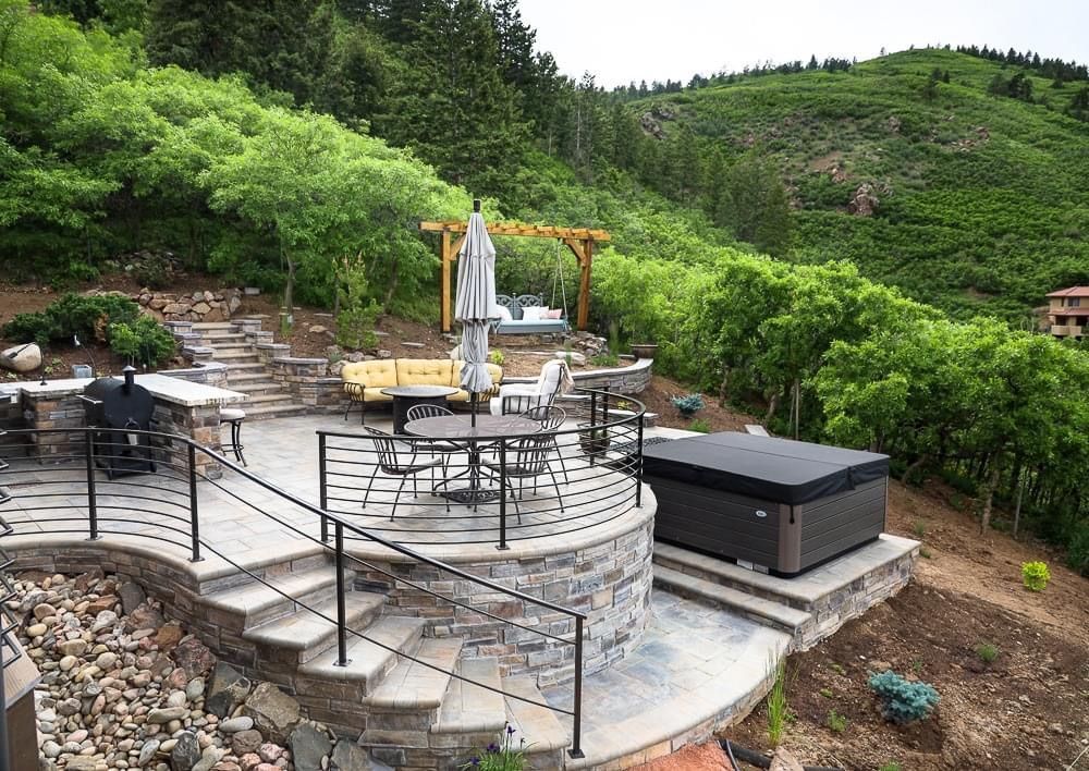 Backyard with a fire pit, three colorful chairs, large tree, and a two-story home in the background.
