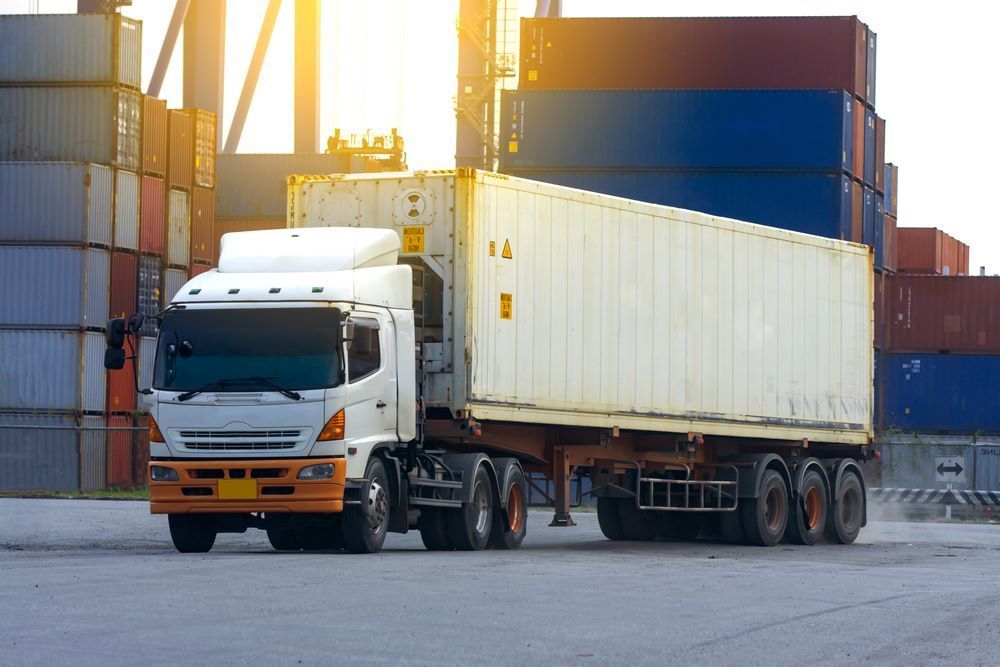 A White Semi Truck is Driving Down a Road Next to a Row of Shipping Containers — Go Pack Yourself in Adelaide, SA