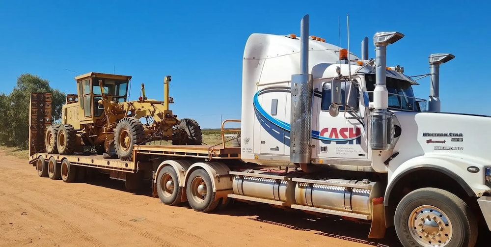 A White Semi Truck Is Carrying A Bulldozer On A Trailer — Go Pack Yourself in Braitling, NT