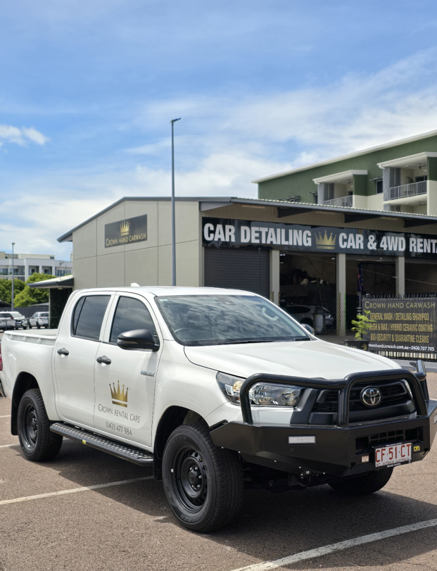 White Toyota Hilux truck parked outside a car detailing and 4WD rental business. — Crown Rental Cars in Nightcliff, NT