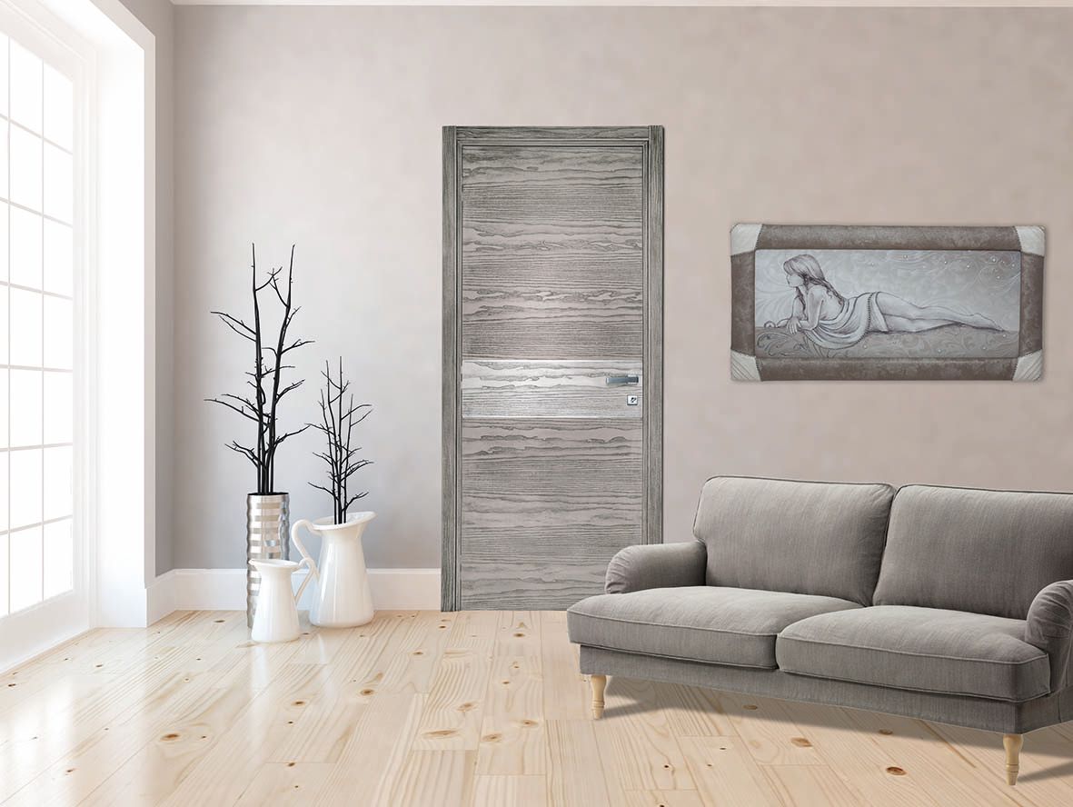 Stanza nei toni del grigio con una porta in legno invecchiato, un divano, opere d'arte e vasi bianchi con rami decorativi.