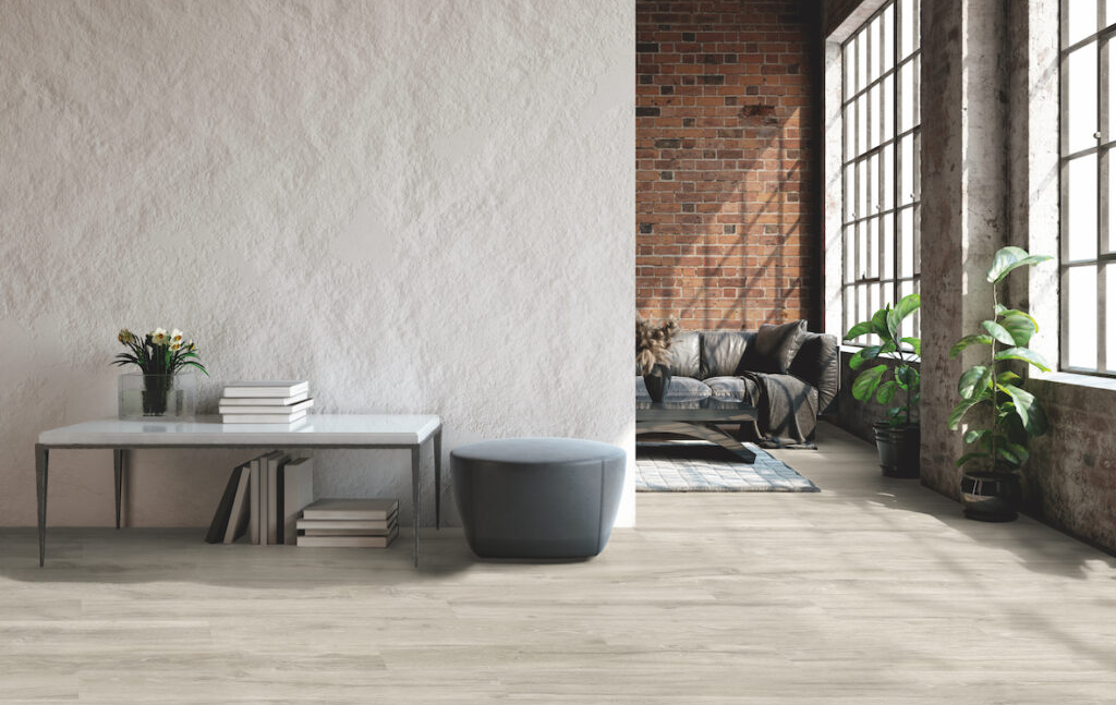 Interno con parete bianca testurizzata, muro di mattoni, piante, divano e pavimento in legno.