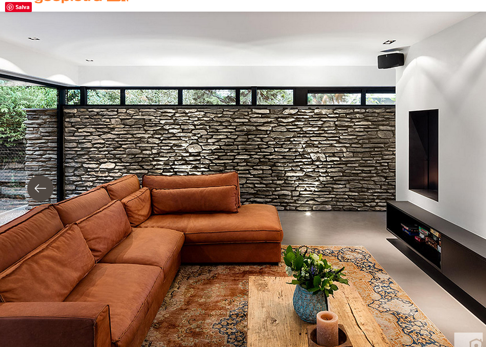 Soggiorno moderno con divano componibile arancione, parete in pietra e consolle bassa nera per l'intrattenimento.