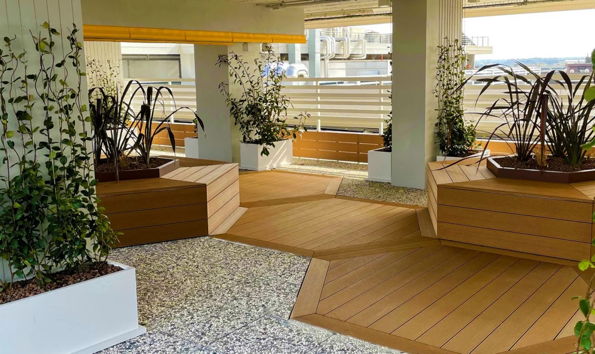 Patio esterno con pavimento esagonale effetto legno, fioriere, ghiaia e piante rampicanti.