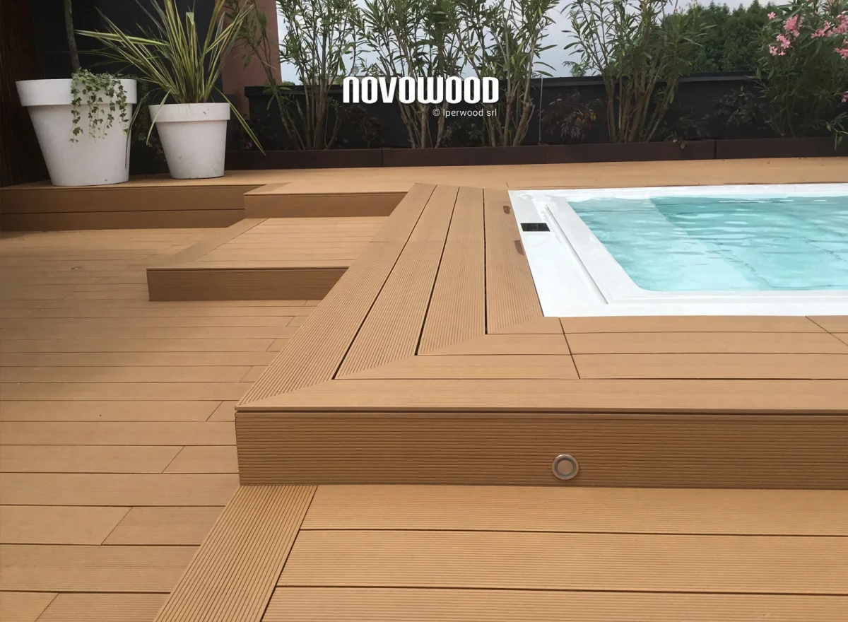 Una terrazza in legno circonda la piscina, con piante sullo sfondo.