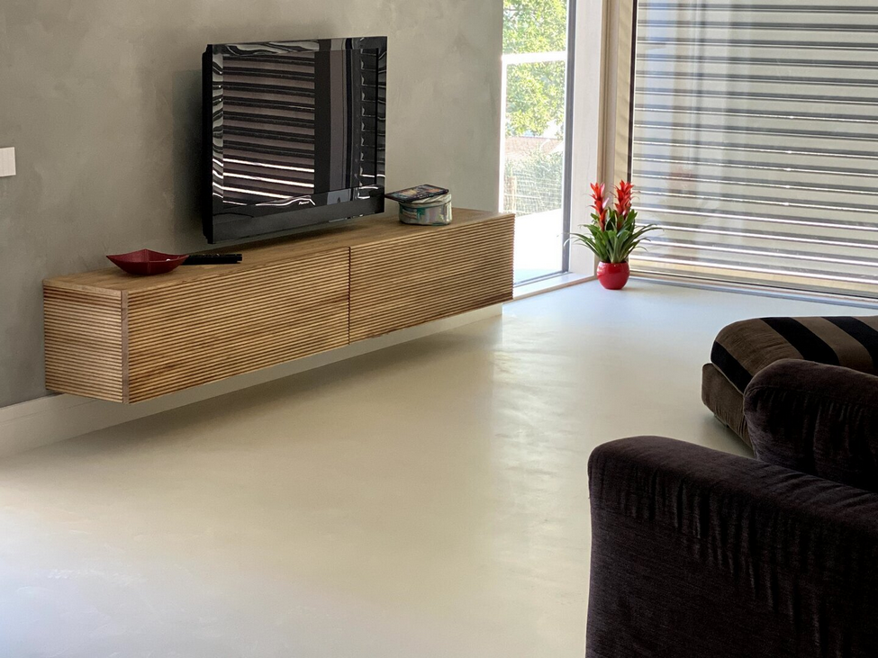 Un mobile porta TV sospeso in legno con una TV su una parete grigia, vicino a una finestra e a un divano.