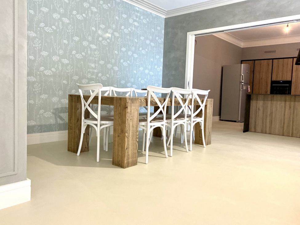 Sala da pranzo con tavolo in legno e sedie bianche, carta da parati floreale azzurra, aperta sulla cucina.