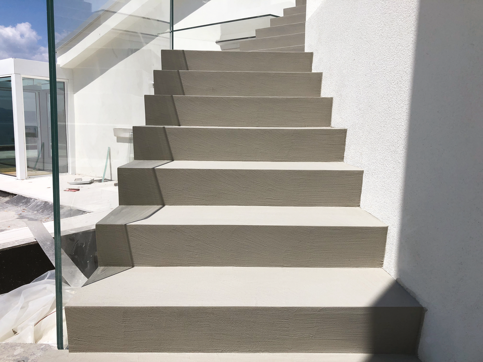 Scala con gradini grigi e pareti bianche che sale. Ringhiera in vetro sulla sinistra.