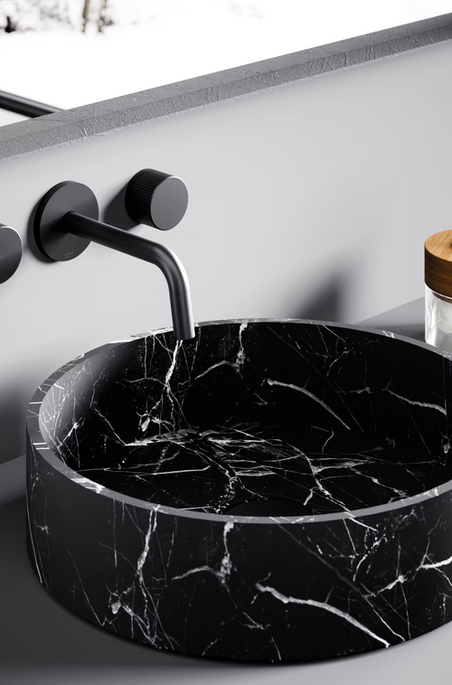 Lavandino in marmo nero con rubinetto e accessori neri opachi montati a parete, su uno sfondo grigio.