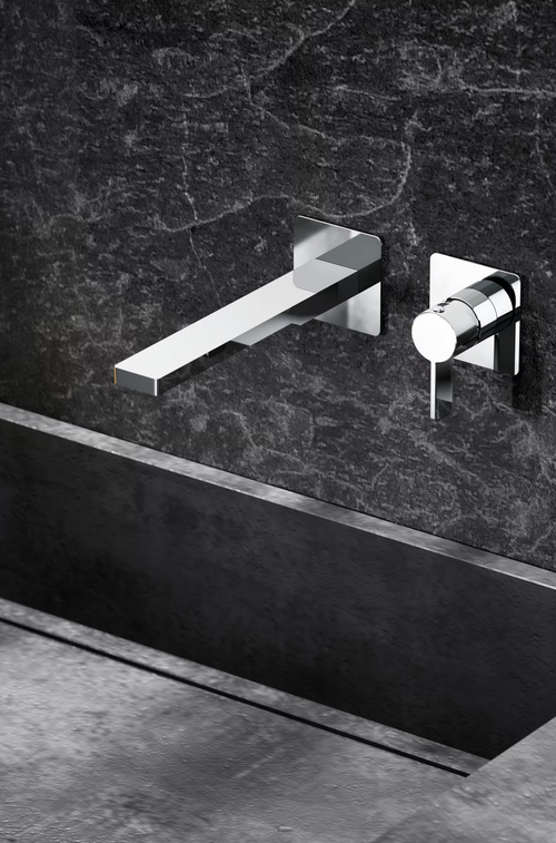 Rubinetti cromati contro una parete in pietra scura, con un lavandino rettangolare nero.