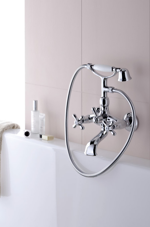 Rubinetto cromato a parete con doccetta. Parete piastrellata beige e vasca da bagno bianca.