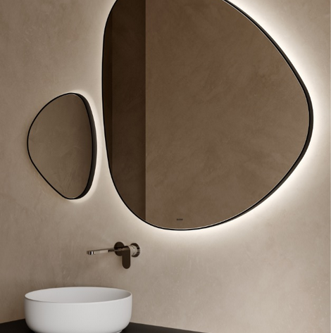 Due specchi irregolari illuminati sopra un lavandino bianco e un mobile scuro in un bagno.