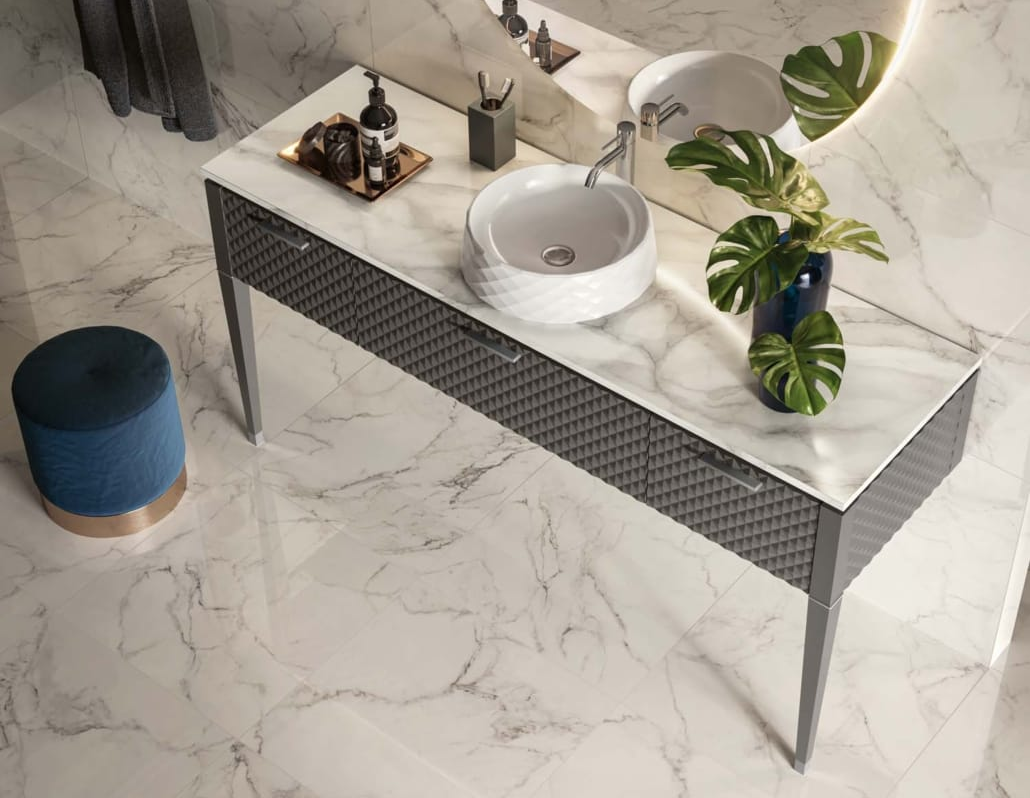 Mobile bagno con piano in marmo e base effetto intrecciato, lavabo bianco e sgabello blu.