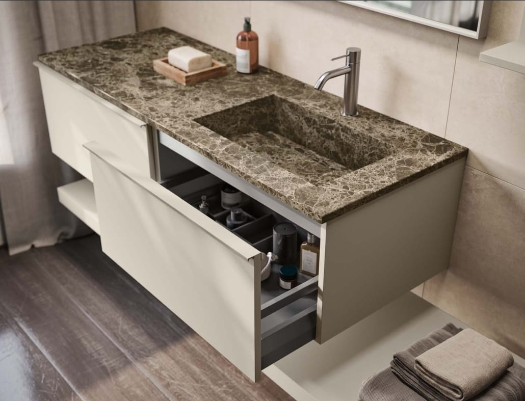 Mobiletto moderno per il bagno con piano in marmo, mobili dai colori chiari e un cassetto aperto.