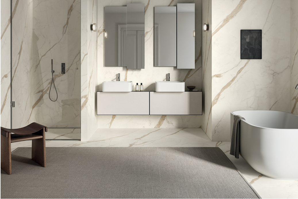 Bagno moderno con pareti effetto marmo, due mobili lavabo sospesi e una vasca da bagno indipendente.