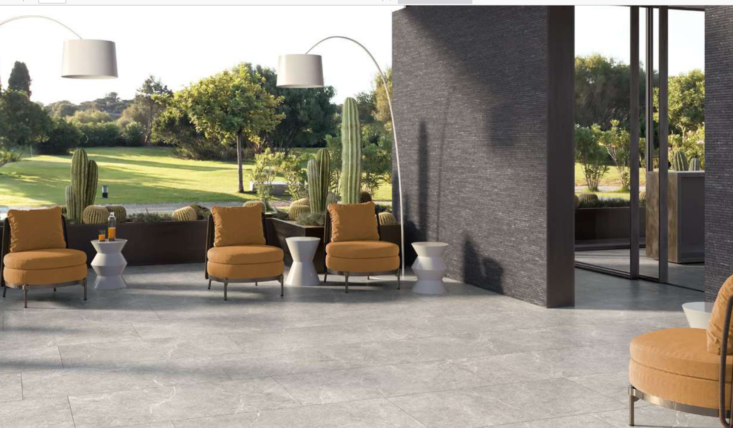 Area salotto all'aperto con poltrone gialle, tavoli bianchi e pavimento grigio con vista sul giardino.