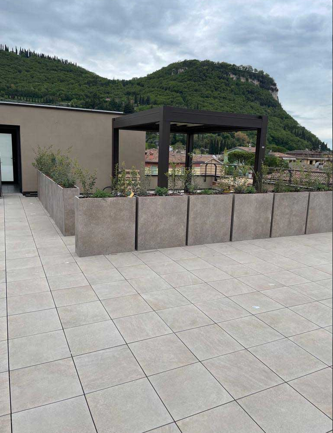 Patio sul tetto con pavimento piastrellato, fioriere, pergolato e montagne sullo sfondo.