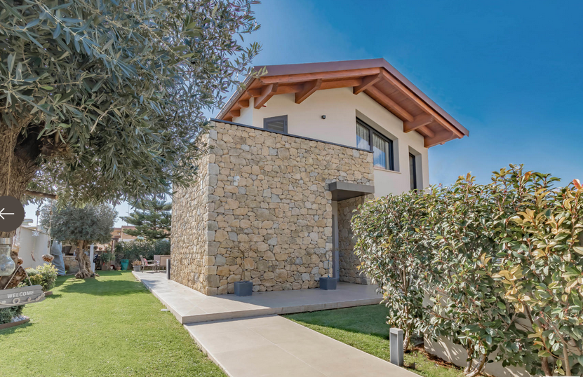 Casa moderna con muro in pietra, prato verde e cielo azzurro.