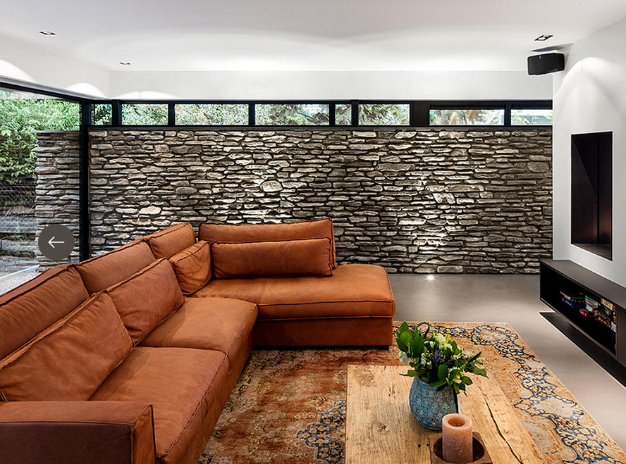 Divano componibile arancione in un soggiorno moderno con parete in pietra.