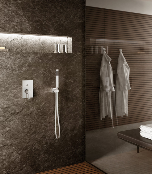 Bagno moderno con parete in pietra scura, mensola incassata, soffione doccia e porta in vetro con due accappatoi.