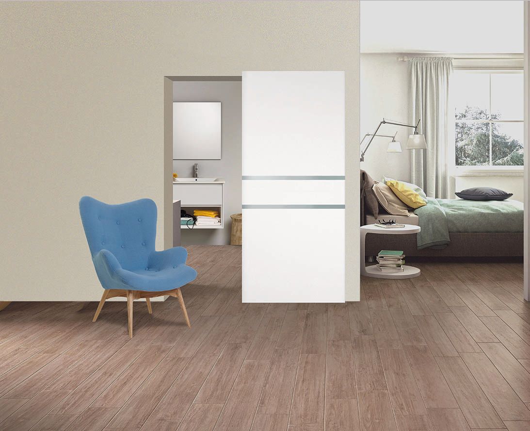 Una stanza con una poltrona blu, una porta scorrevole e una camera da letto visibile al di là. Pavimenti in legno.