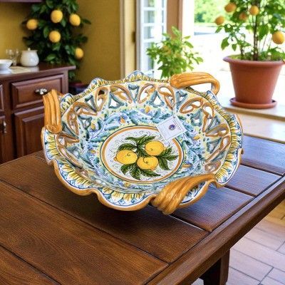 Ciotola decorativa in ceramica con motivo a limoni, posta su un tavolo di legno. Tonalità di giallo, blu e marrone.