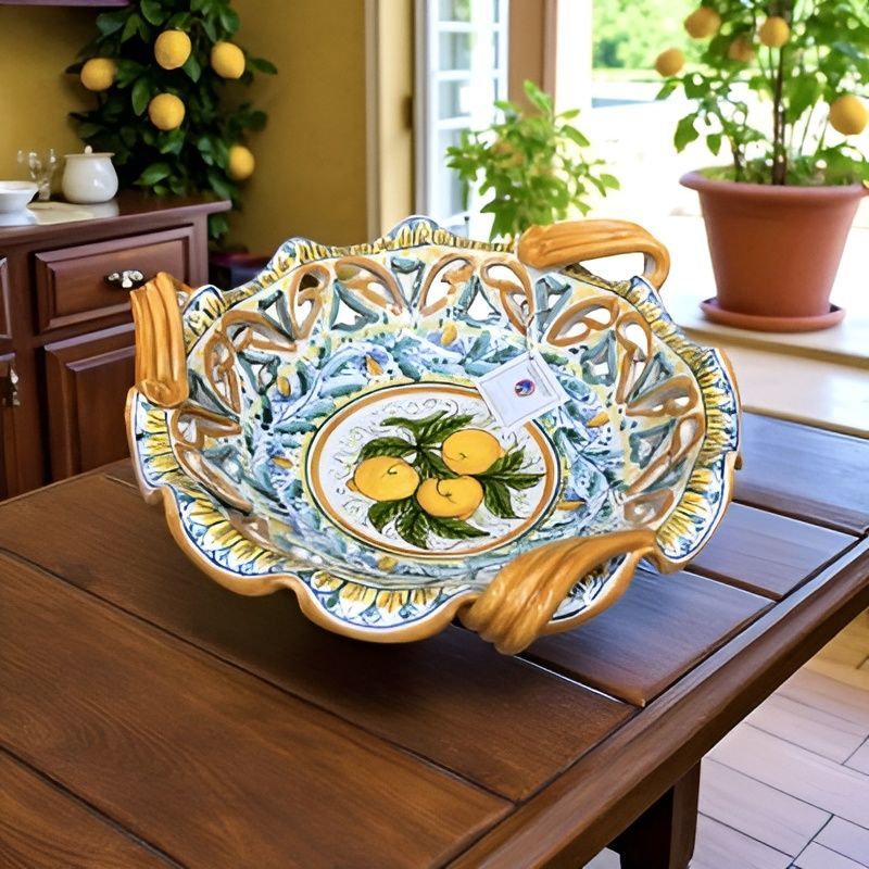 Ciotola decorativa in ceramica con motivo a limoni, posta su un tavolo di legno, con alberi di limoni sullo sfondo.