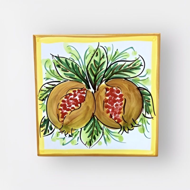 Piastrella in ceramica dipinta raffigurante due melograni con foglie verdi su sfondo giallo, incorniciati in oro.