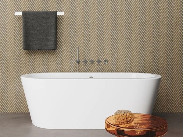 Vasca da bagno bianca contro una parete con motivo a spina di pesce e asciugamano grigio.