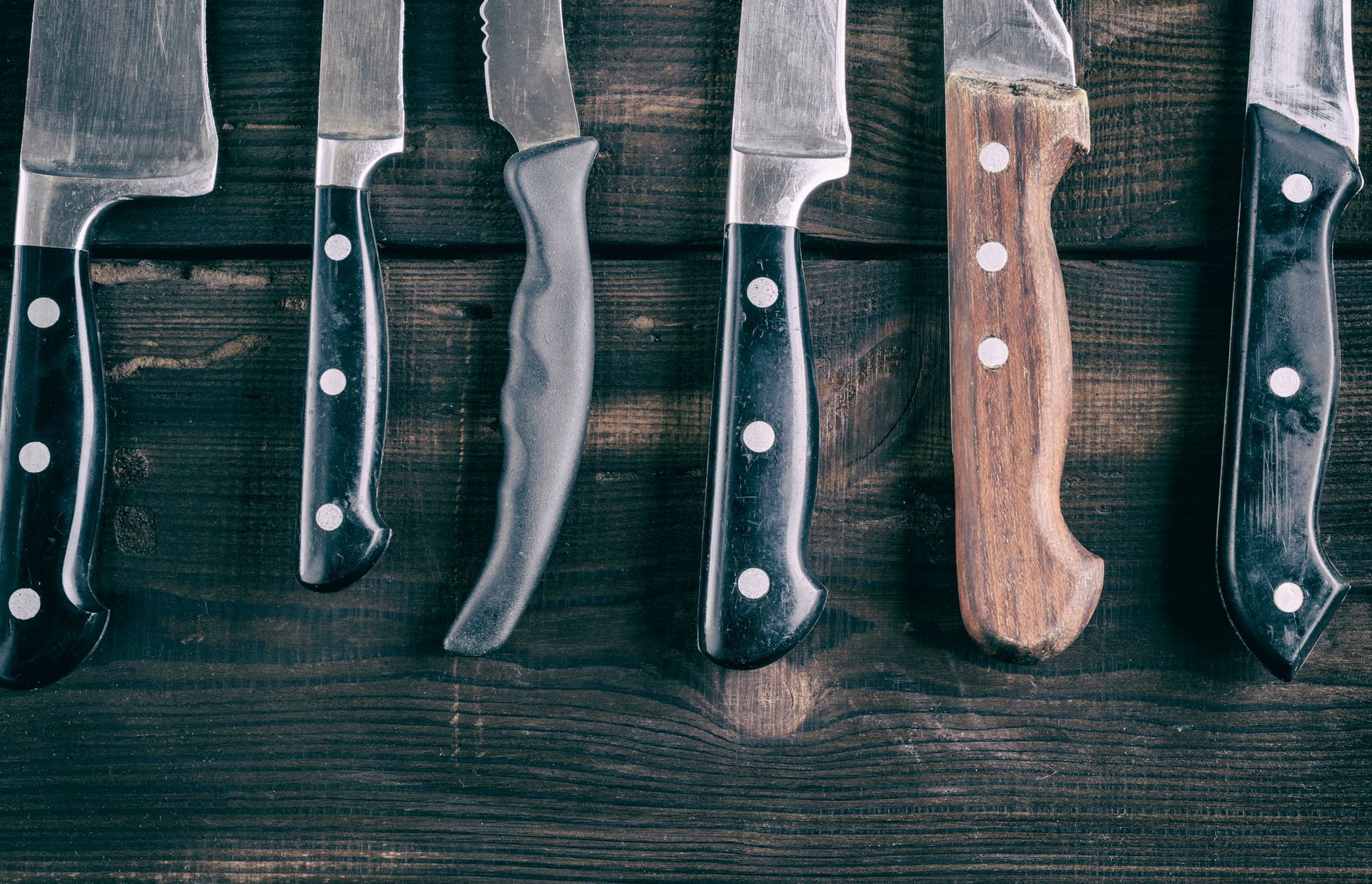 A row of knives are lined up on a wooden table.