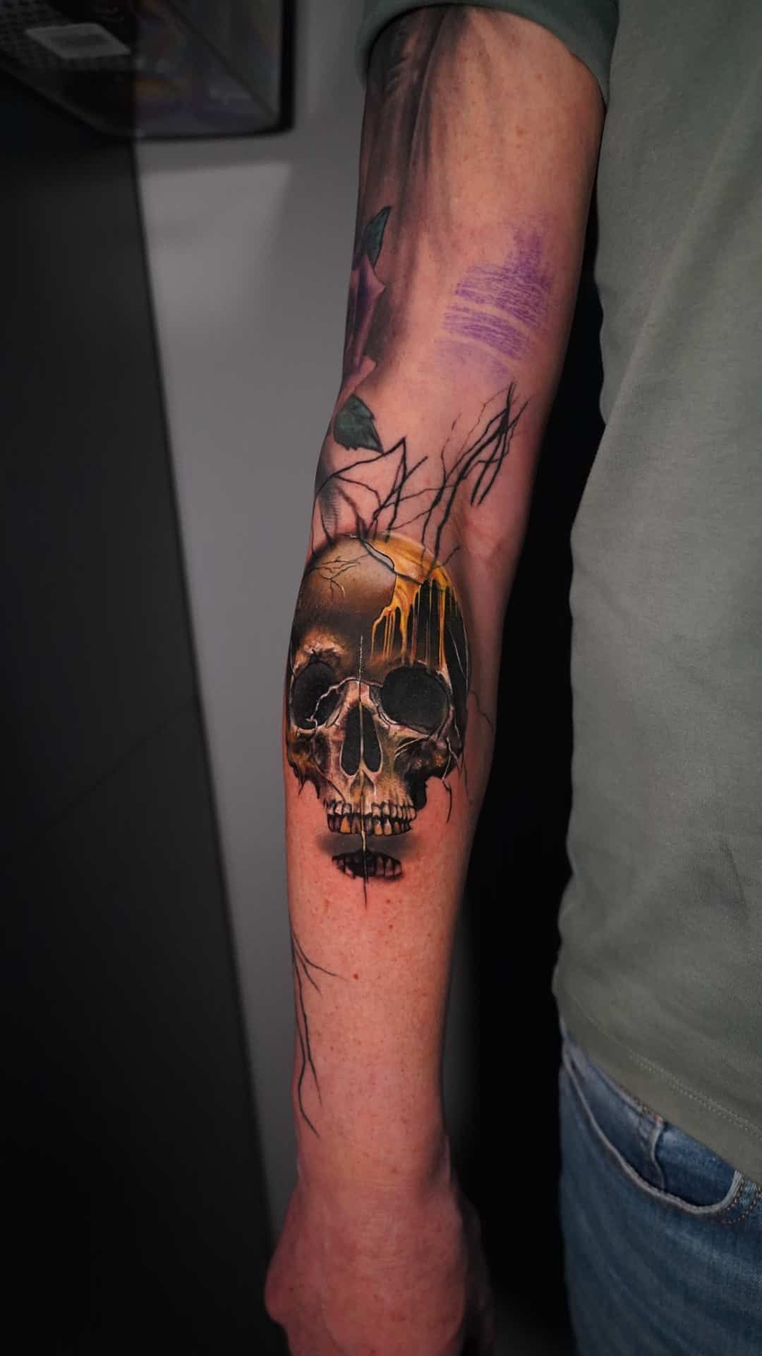 A close-up of a forearm tattoo featuring a realistic, monochromatic skull with a vibrant yellow glow above it.