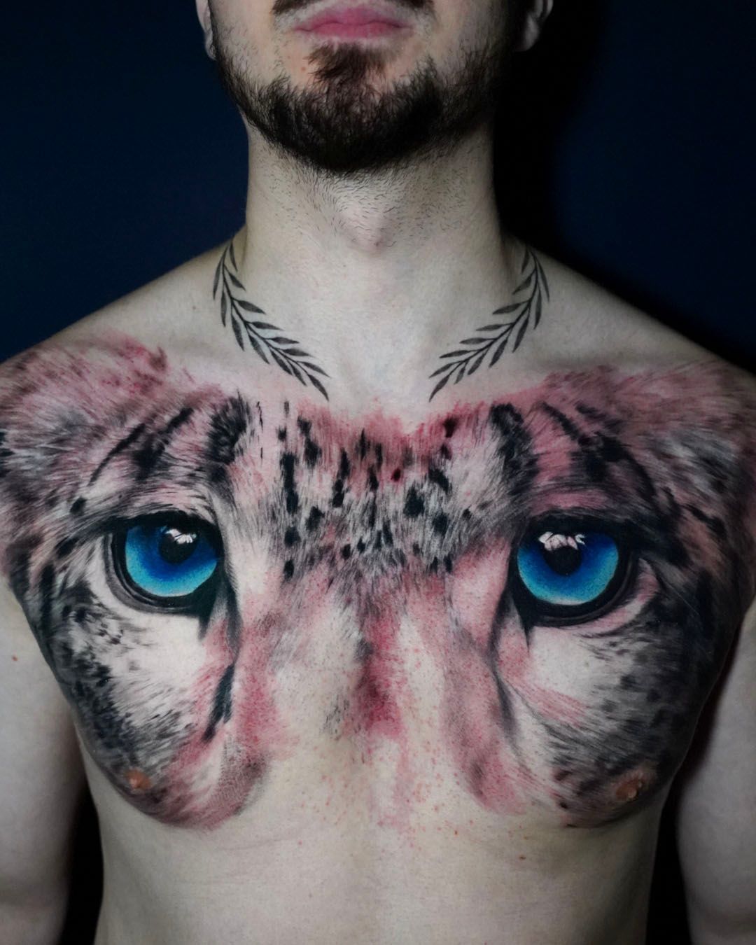 Chest tattoo of a snow leopard’s face with piercing blue eyes, plus a laurel wreath design around the neck.