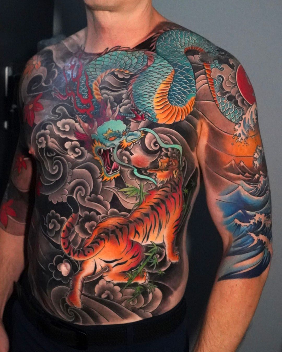 Torso and shoulder tattoo featuring a vibrant orange tiger battling a blue dragon amidst black and grey swirling clouds.