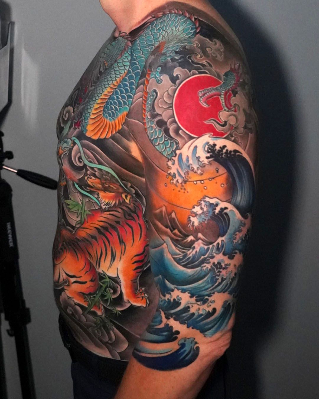 A person with a detailed Japanese-style tattoo on their shoulder and chest featuring a dragon, tiger, and ocean waves.
