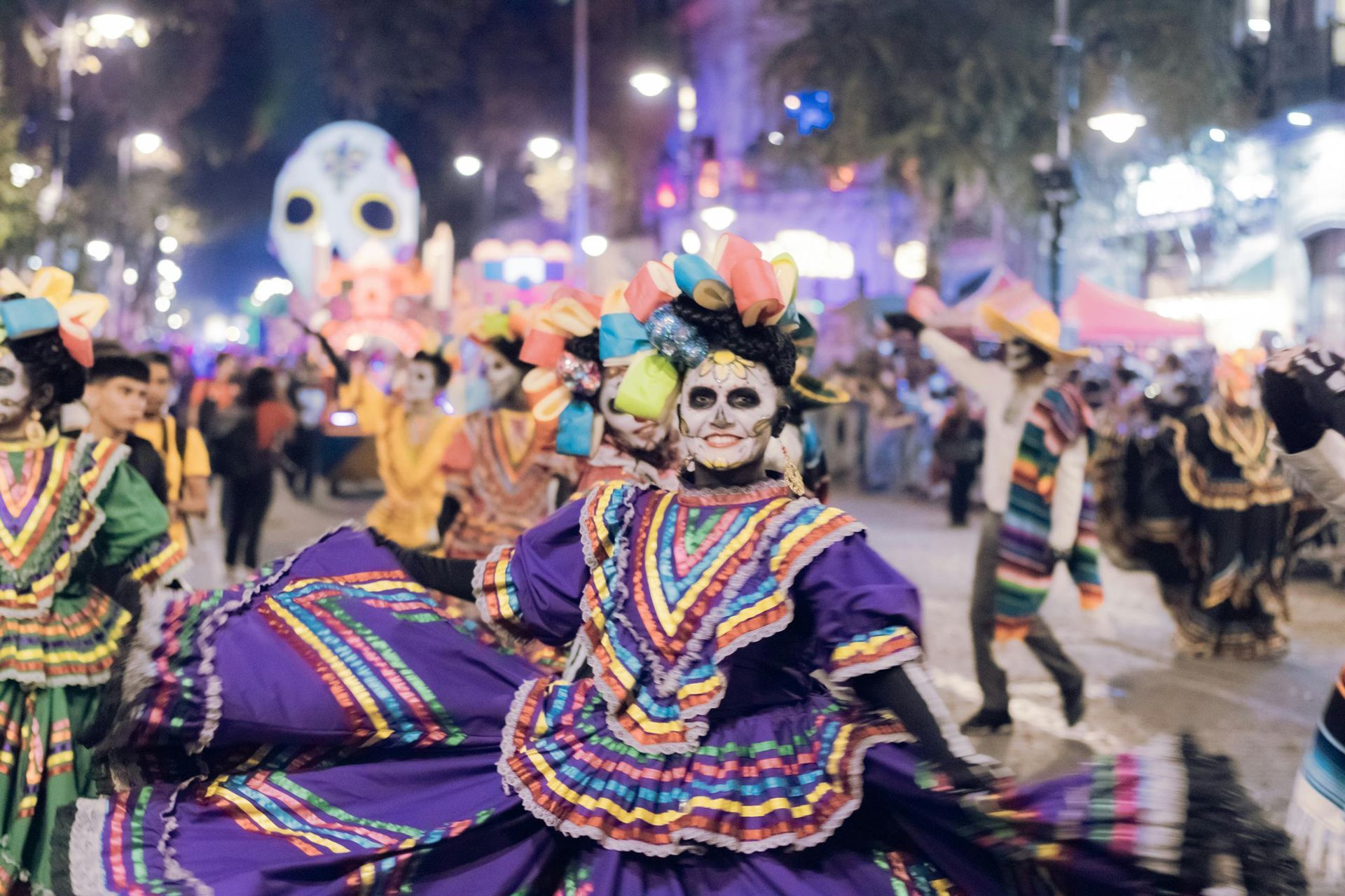 Day of the Dead parade with dancers in elaborate costumes, makeup, and a giant skull float.